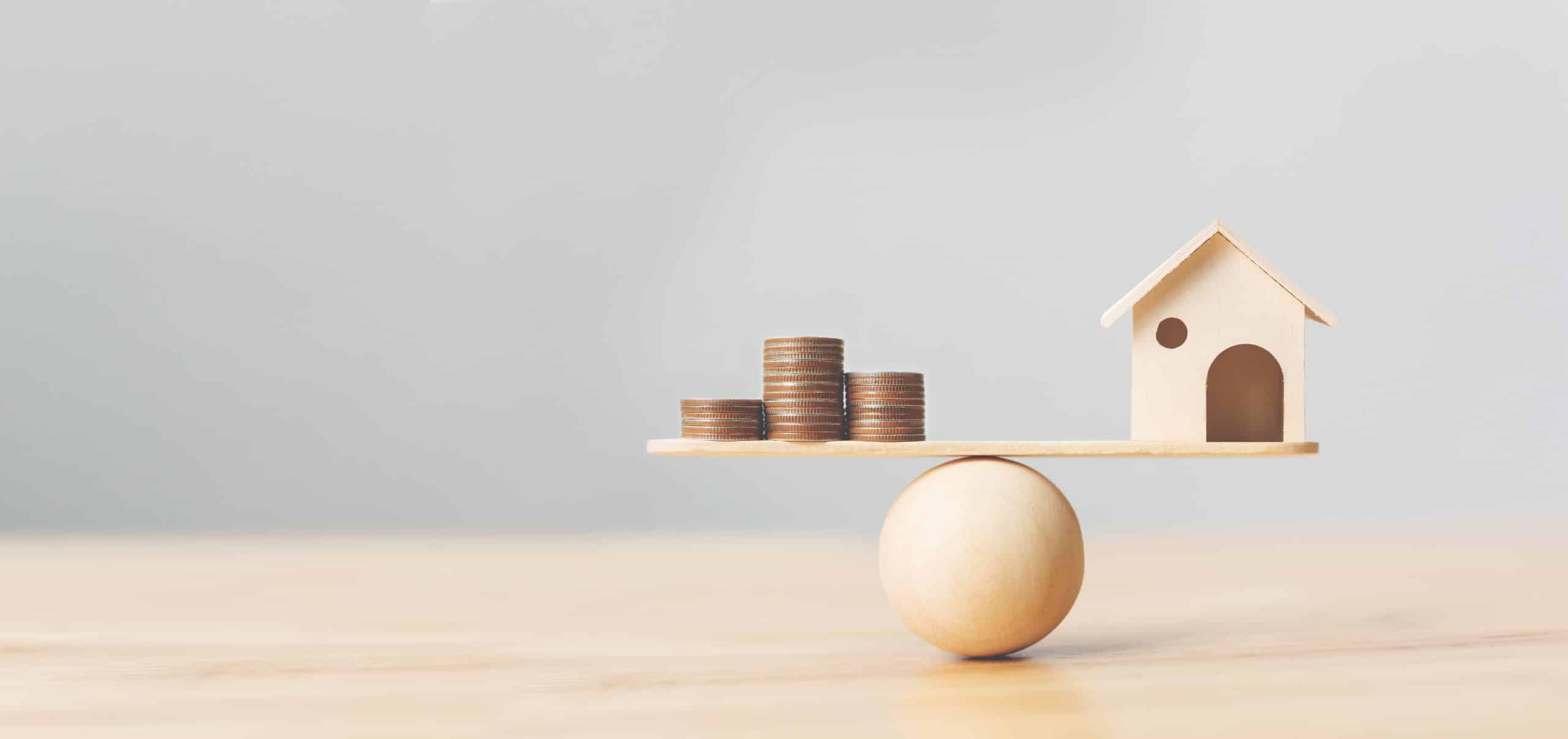 coins and a toy house in a balance
