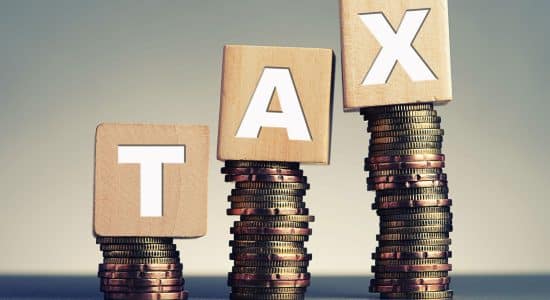 tax in wooden blocks on top of a stack of coins